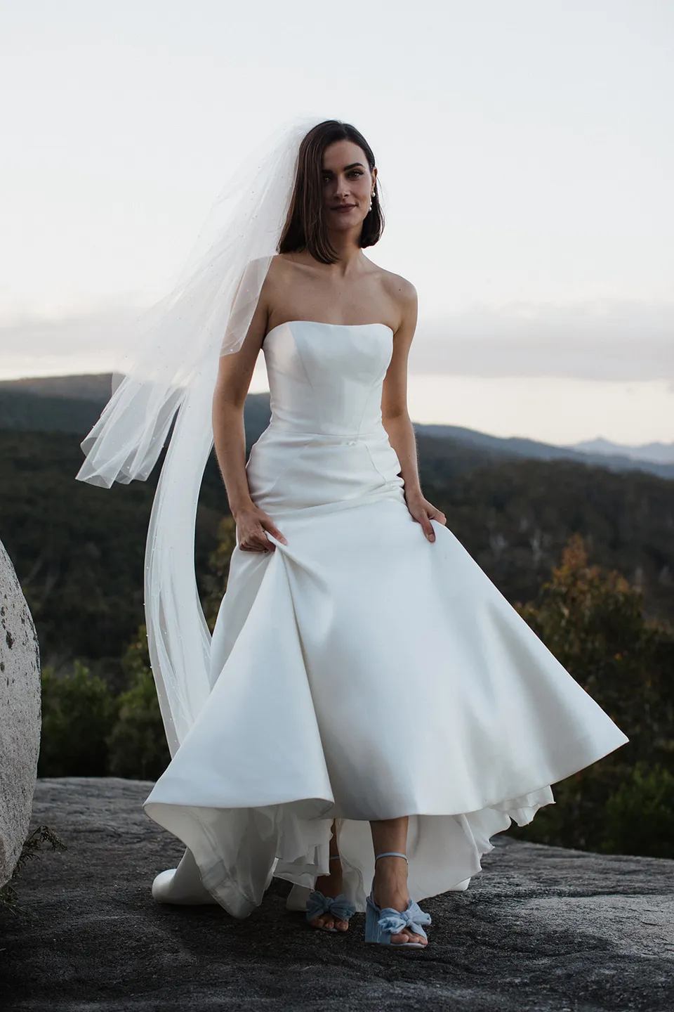 Meg standing on the rocks as the breeze lifts her veil and the hem of her wedding dress. At The Keep on Tasmania’s east coast, for an Elopement Collective elopement. Photograph by Jenna Agius.