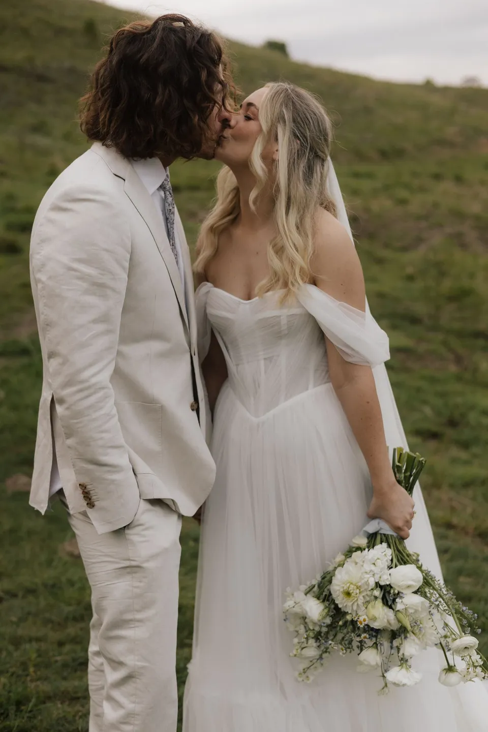 Bridget smiling up at James as they stand close together in the paddock. At Cudgera Creek in northern New South Wales, for an Elopement Collective elopement. Photograph by Bulb Creative.