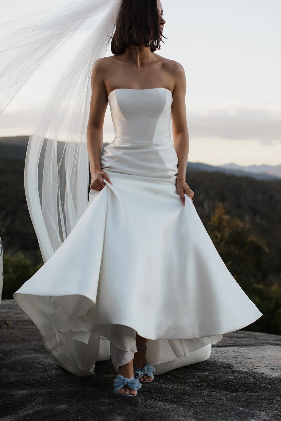 Meg holding the sides of her wedding dress, with blue shoes peeking beneath its moving hem. At The Keep on Tasmania’s east coast, for an Elopement Collective elopement. Photograph by Jenna Agius.