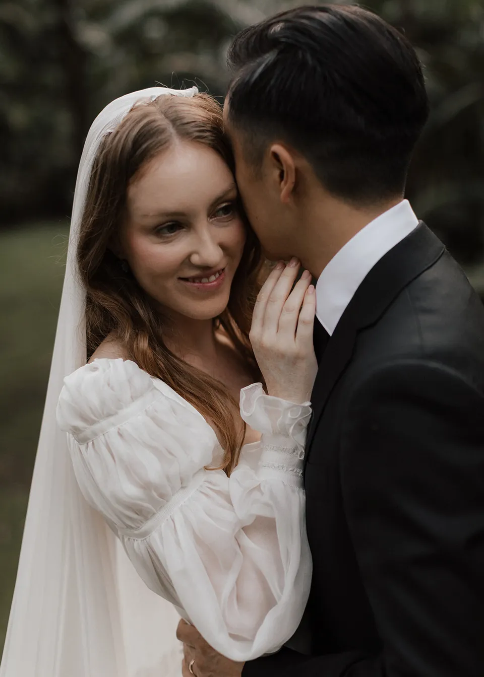Elyse smiling as Jonathan leans close to her face. At Fig Tree Villa in Ewingsdale, Byron Bay, for an Elopement Collective elopement. Photograph by Bulb Creative.
