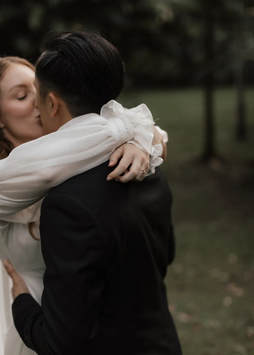 Elyse wrapping her arms around Jonathan's shoulders for a kiss. At Fig Tree Villa in Ewingsdale, Byron Bay, for an Elopement Collective elopement. Photograph by Bulb Creative.