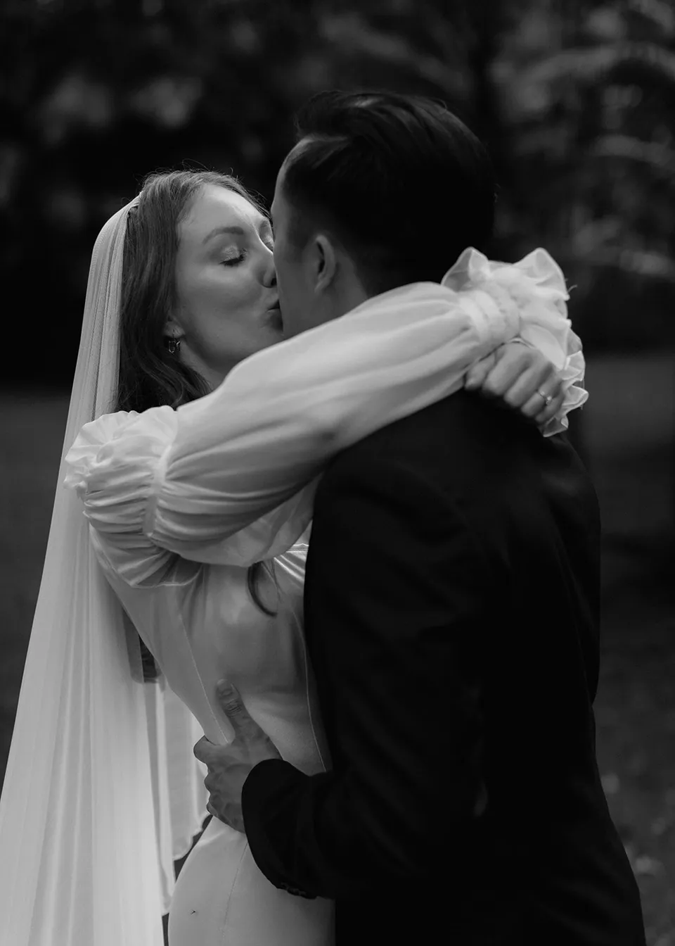 Black-and-white detail of Elyse's arms around Jonathan as they kiss. At Fig Tree Villa in Ewingsdale, Byron Bay, for an Elopement Collective elopement. Photograph by Bulb Creative.