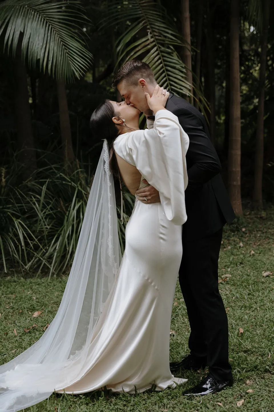 Matthew embracing Laura beneath the palms after their ceremony. At Fig Tree Villa in Ewingsdale, Byron Bay, for an Elopement Collective elopement. Photograph by George Bowden.