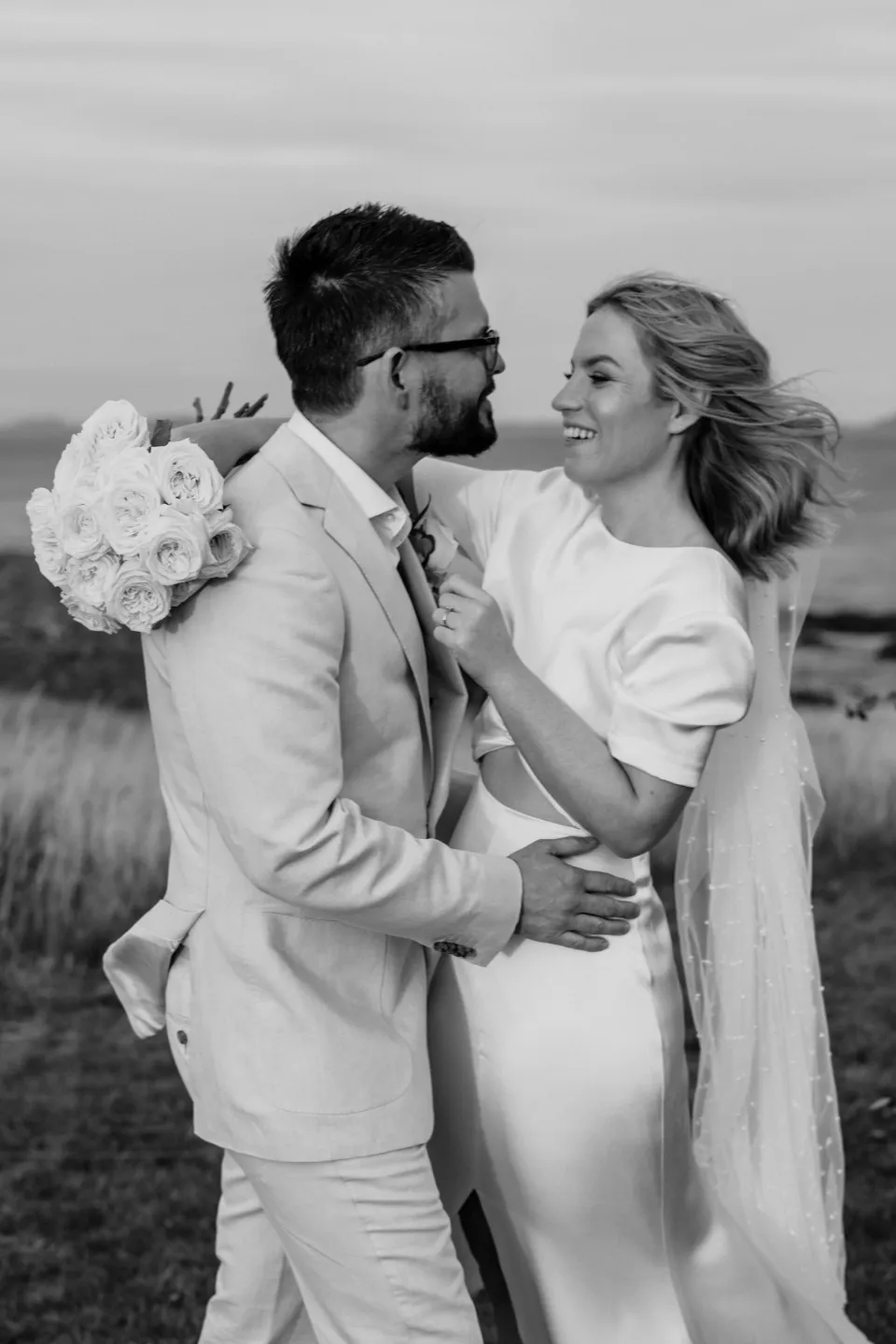 Black and white portrait of Jemmah and Jack smiling at each other, at Thalia Haven on the East Coast of Tasmania, Australia, for an Elopement Collective elopement. Photograph by Joey Willis.