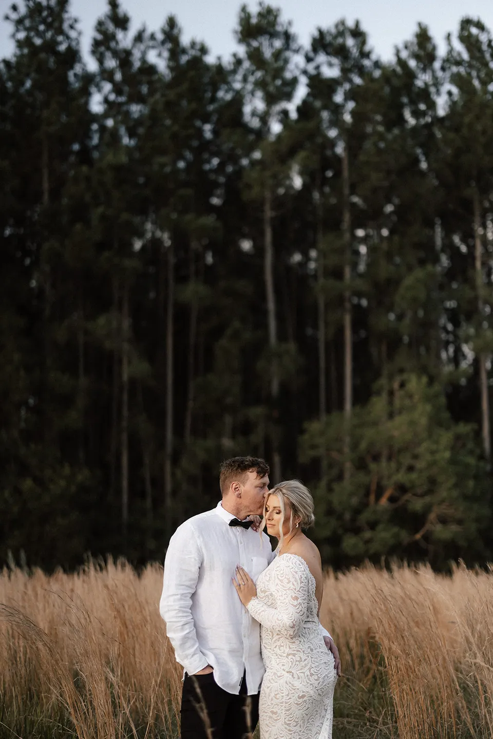 Matt and Laura kissing among dry grasses beneath tall trees, in the Tweed Valley, NSW, for an Elopement Collective elopement. Photo by Bulb Creative.