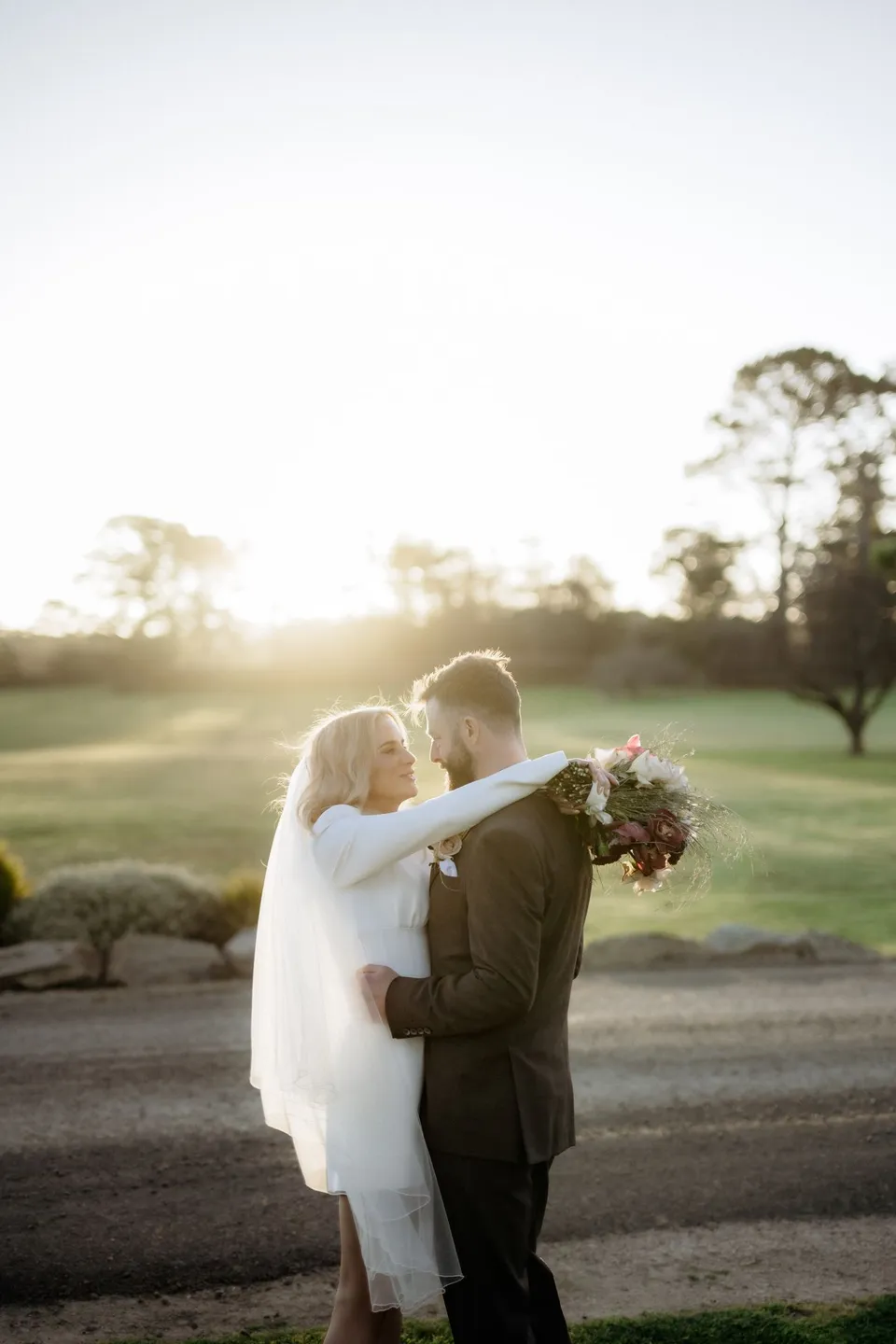 A couple embracing in low golden light at Piermont Retreat on Tasmania’s east coast, photographed by Omar of By The Wilde for an Elopement Collective elopement.