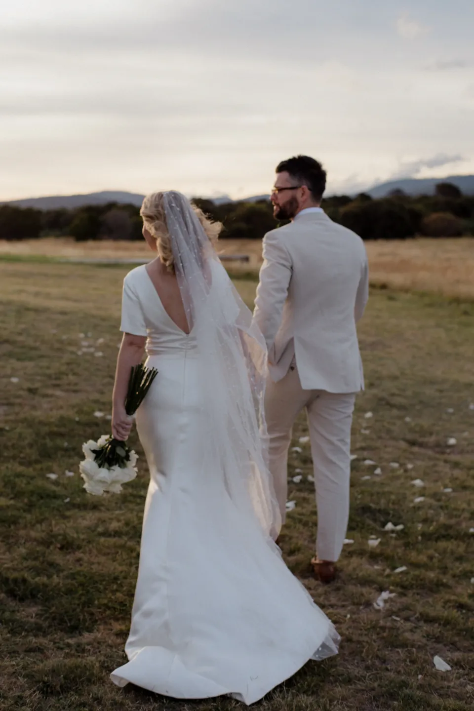Jack looking back as the couple walk across the meadow, at Thalia Haven on the East Coast of Tasmania, Australia, for an Elopement Collective elopement. Photograph by Joey Willis.
