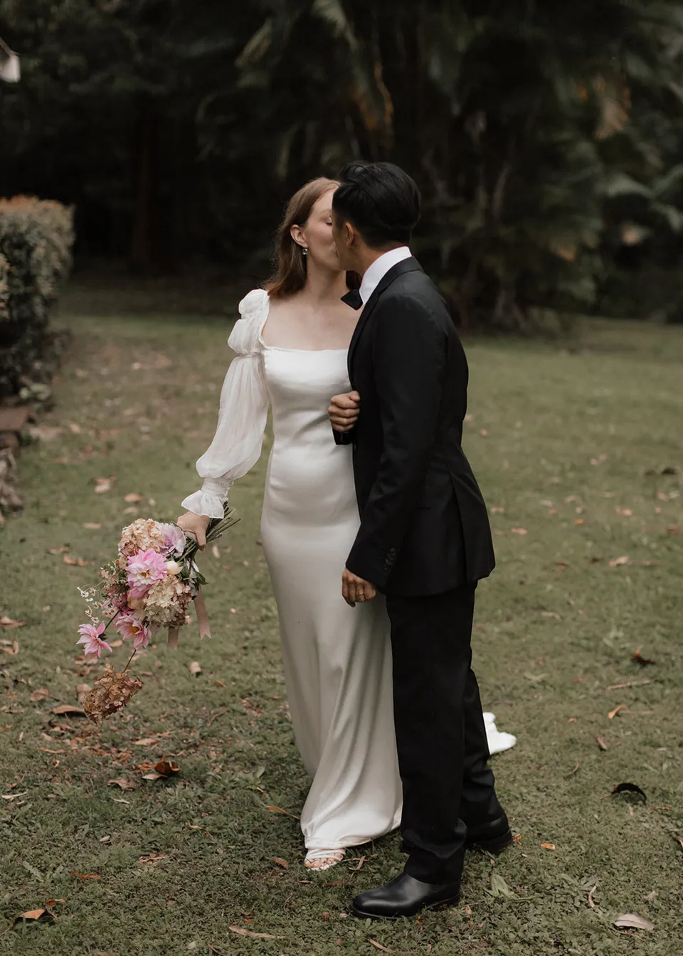 Jonathan kissing Elyse's temple while she holds her bouquet at her side, with flowers by The Perfect Party Co. At Fig Tree Villa in Ewingsdale, Byron Bay, for an Elopement Collective elopement. Photograph by Bulb Creative.
