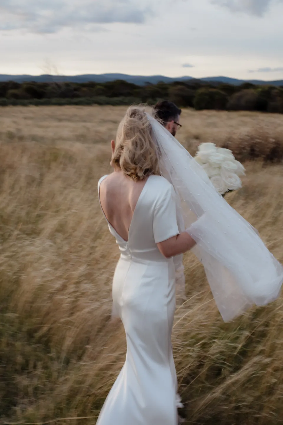 Jemmah’s long veil lifting above the golden grass, at Thalia Haven on the East Coast of Tasmania, Australia, for an Elopement Collective elopement. Photograph by Joey Willis.