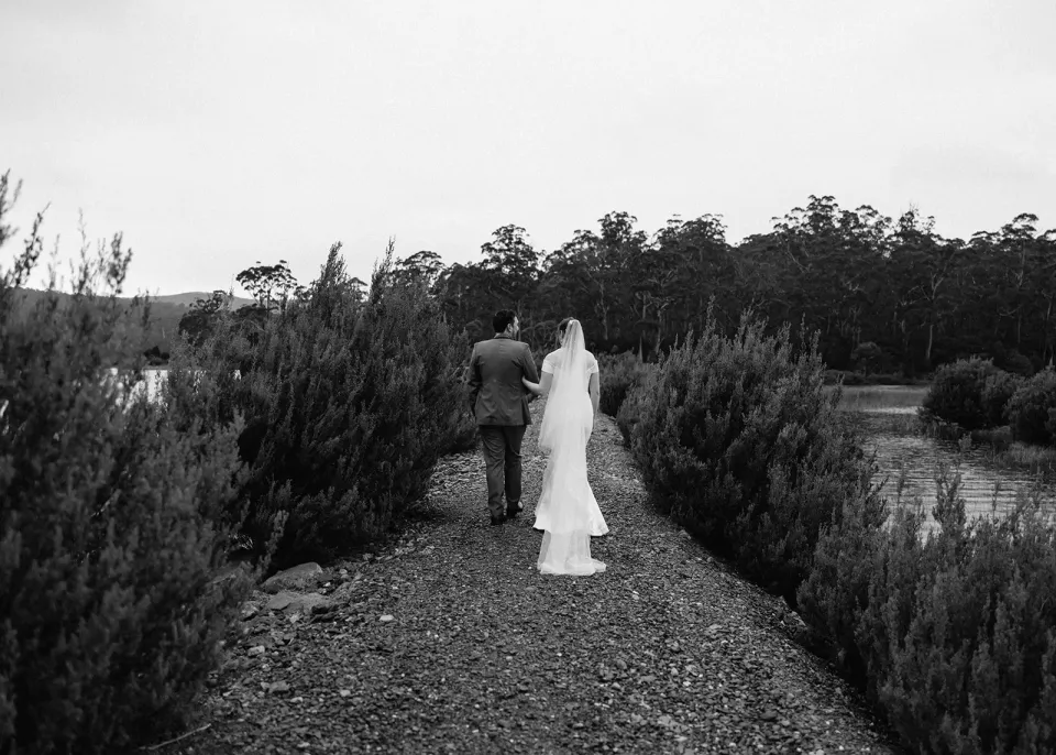 A black-and-white photograph of a couple walking along a rocky path through lakeside scrub.