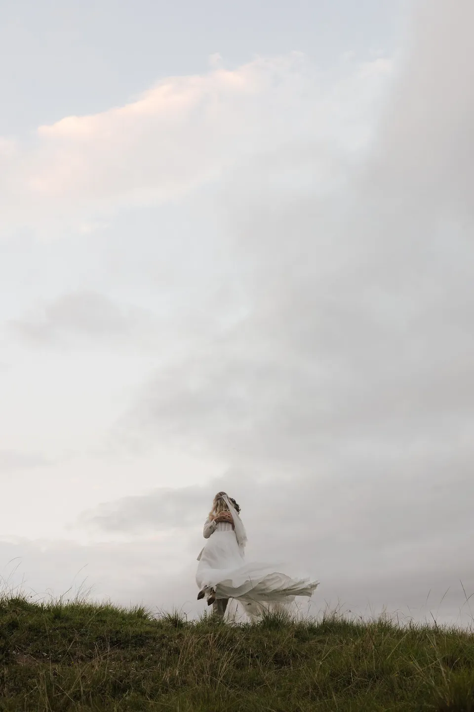 Bridget's veil streaming in the breeze as she stands on the grassy hill. At Cudgera Creek in northern New South Wales, for an Elopement Collective elopement. Photograph by Bulb Creative.