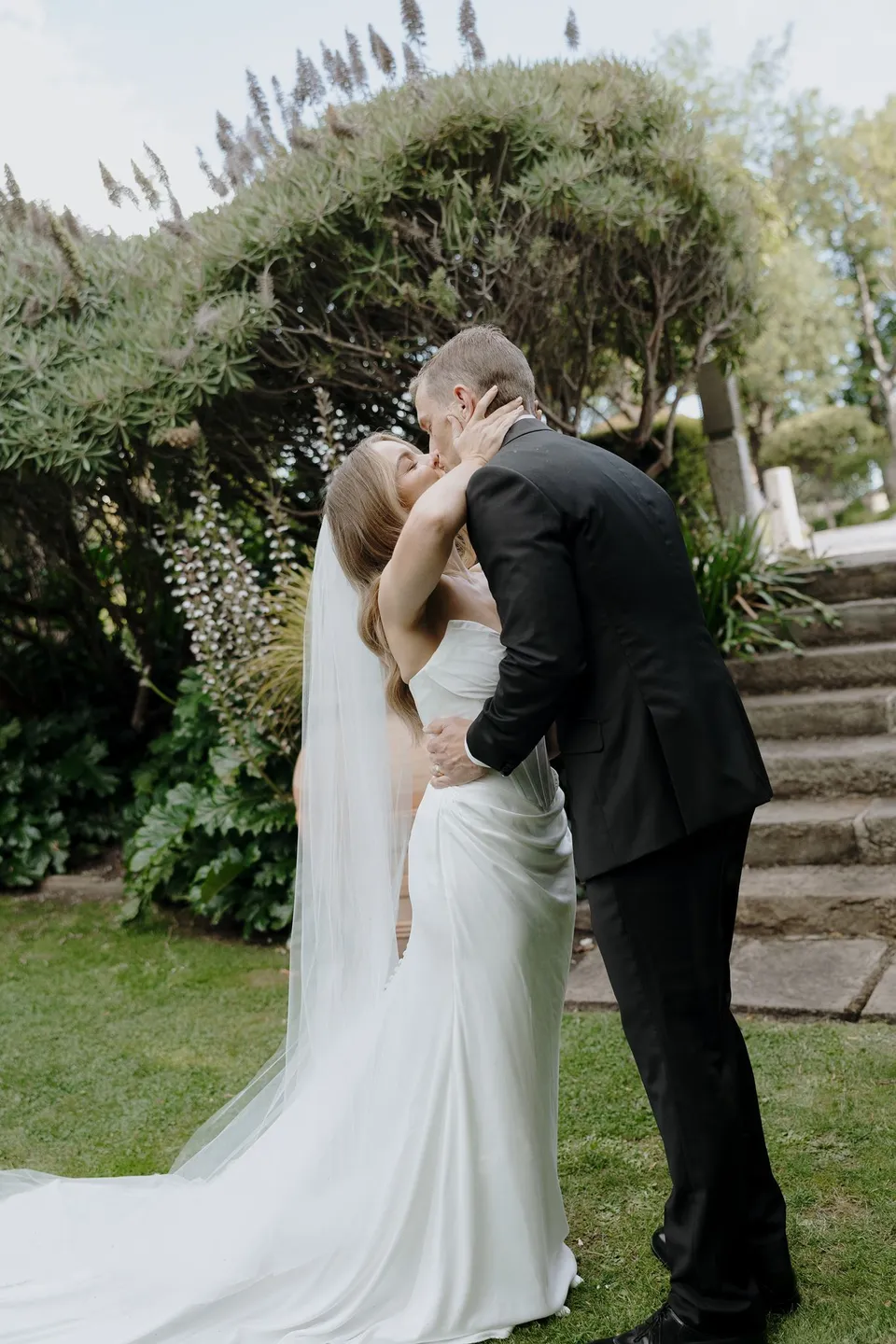 Tanesha and Andrew kissing during their ceremony beneath the garden trees, at Islington Hotel in South Hobart, Tasmania, Australia, for an Elopement Collective summer elopement. Photograph by George Bowden.