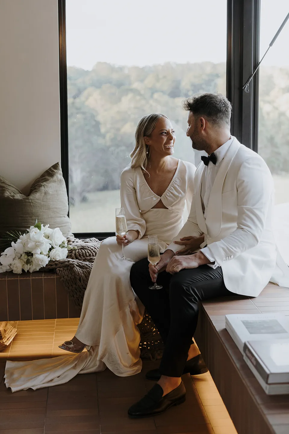 Gabrielle and Greg sitting close together on the cabin’s window seat with her bouquet beside them at Roundhill Retreat in Obi Obi, Sunshine Coast Hinterland, for their Elopement Collective elopement.
