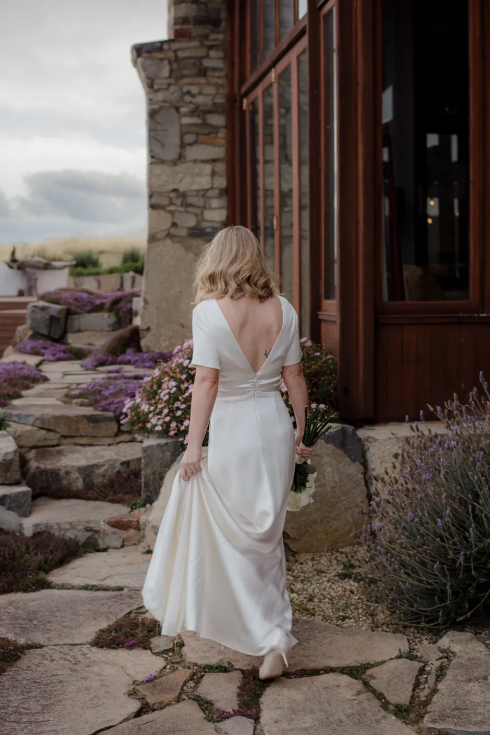 Jemmah walking down stone steps beside timber-framed windows, at Thalia Haven on the East Coast of Tasmania, Australia, for an Elopement Collective elopement. Photograph by Joey Willis.