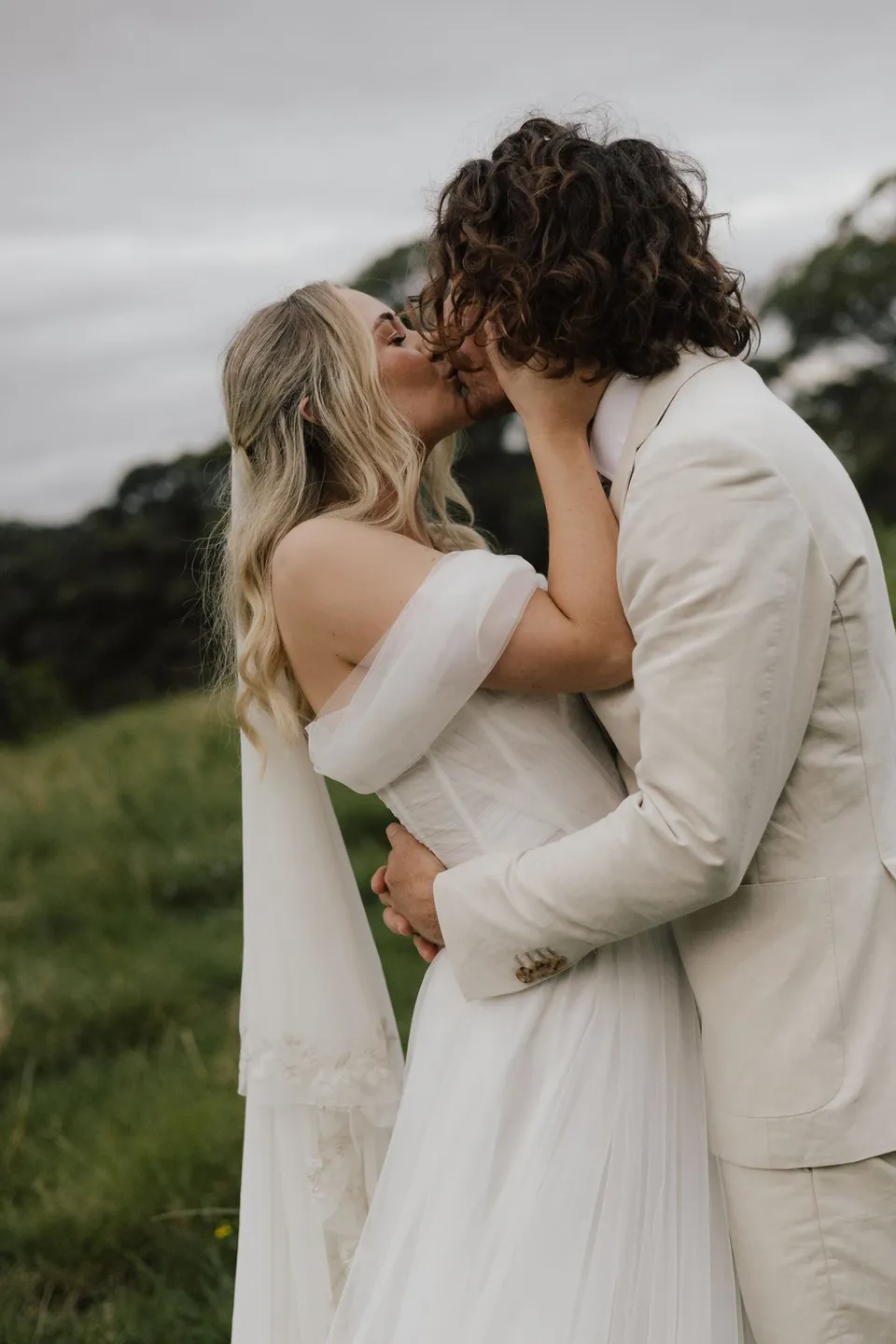 Bridget reaching up to James as they kiss in the paddock. At Cudgera Creek in northern New South Wales, for an Elopement Collective elopement. Photograph by Bulb Creative.