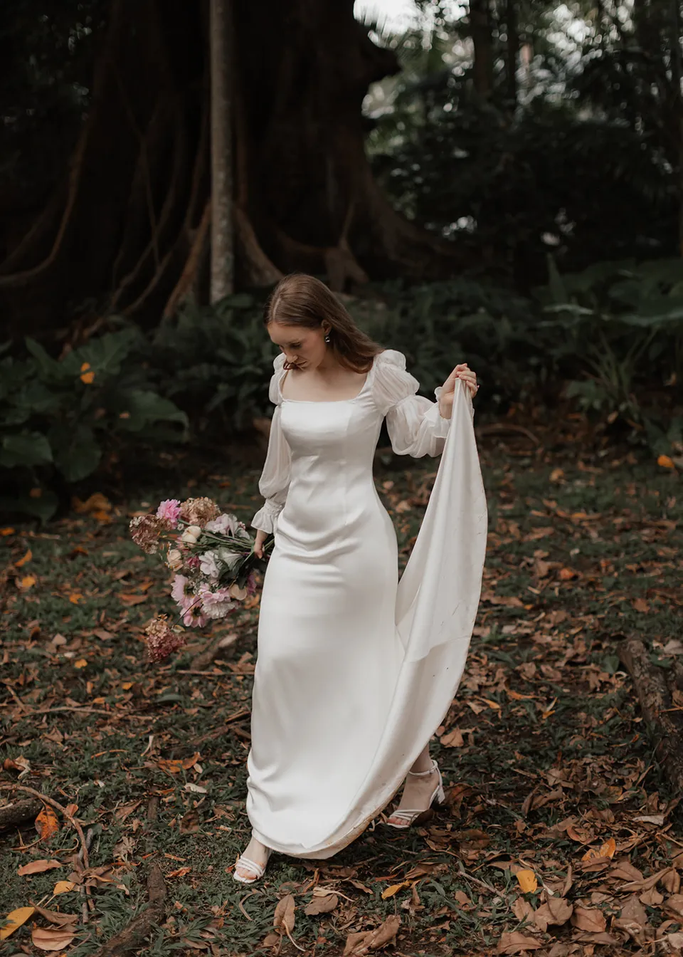 Elyse gathering her veil as she walks across fallen leaves. At Fig Tree Villa in Ewingsdale, Byron Bay, for an Elopement Collective elopement. Photograph by Bulb Creative.