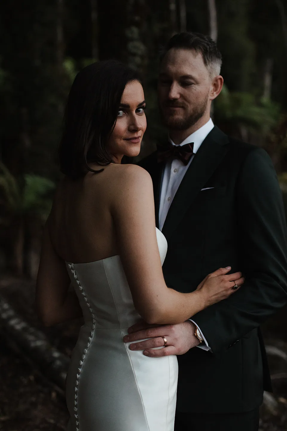 Close portrait of Meg and Ryan holding each other in the fern-filled forest. At The Keep on Tasmania’s east coast, for an Elopement Collective elopement. Photograph by Jenna Agius.