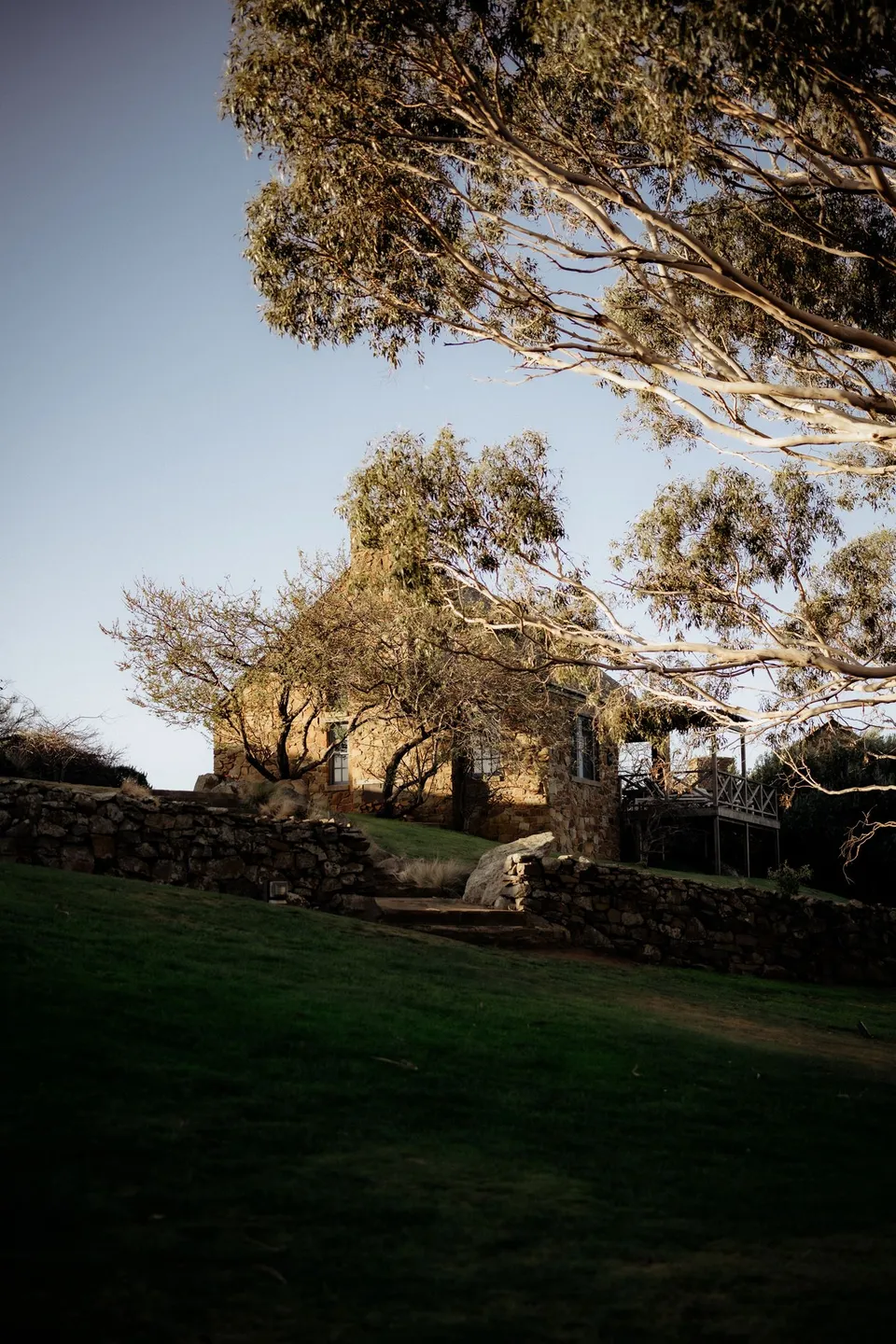A stone cottage and terraced garden framed by trees in warm low sunlight. At Piermont Retreat on Tasmania’s east coast, for an Elopement Collective elopement. Photograph by Omar of By The Wilde.