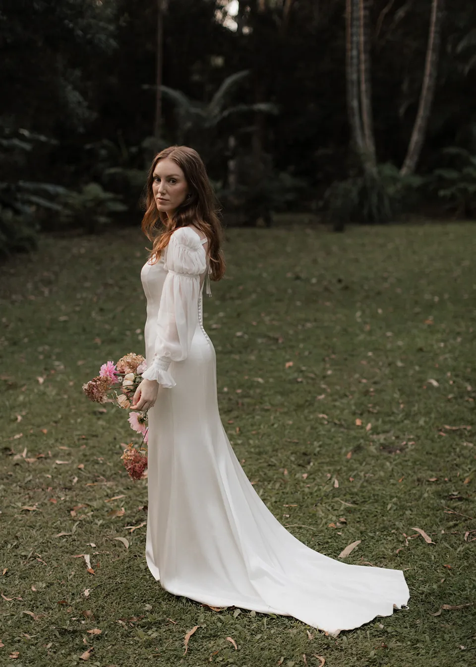 Elyse turning towards the camera with her dress train across the grass. At Fig Tree Villa in Ewingsdale, Byron Bay, for an Elopement Collective elopement. Photograph by Bulb Creative.