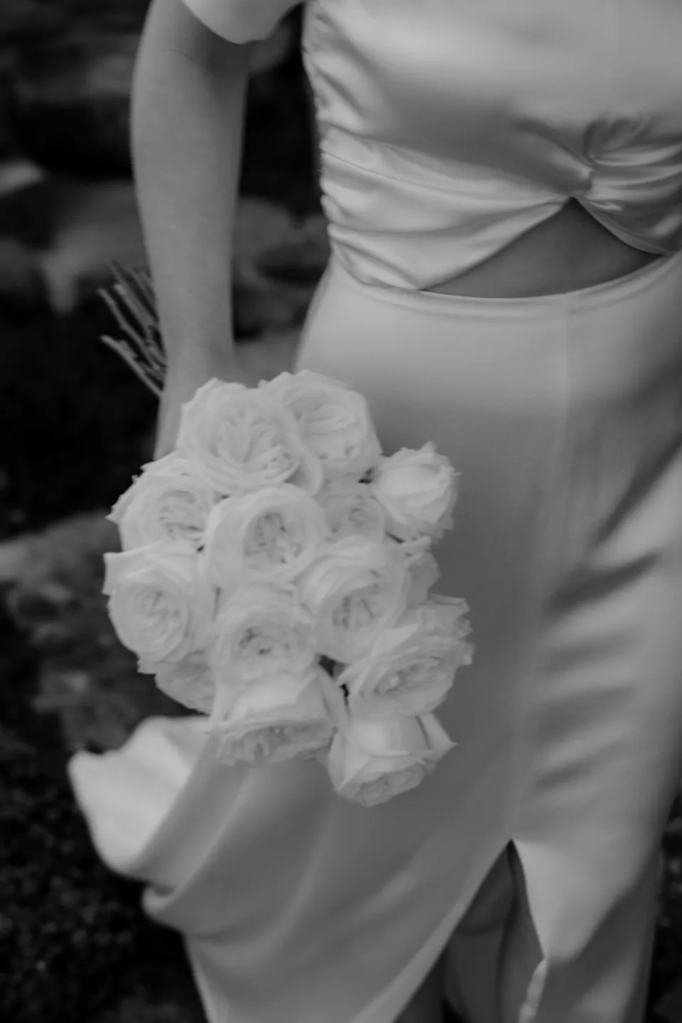 Black and white close-up of Jemmah’s white rose bouquet by The Romantics, at Thalia Haven on the East Coast of Tasmania, Australia, for an Elopement Collective elopement. Photograph by Joey Willis.