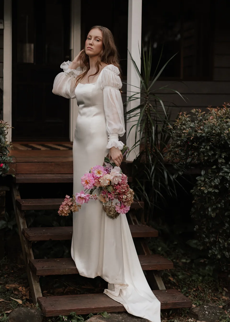 Elyse brushing back her hair beside the verandah. At Fig Tree Villa in Ewingsdale, Byron Bay, for an Elopement Collective elopement. Photograph by Bulb Creative.