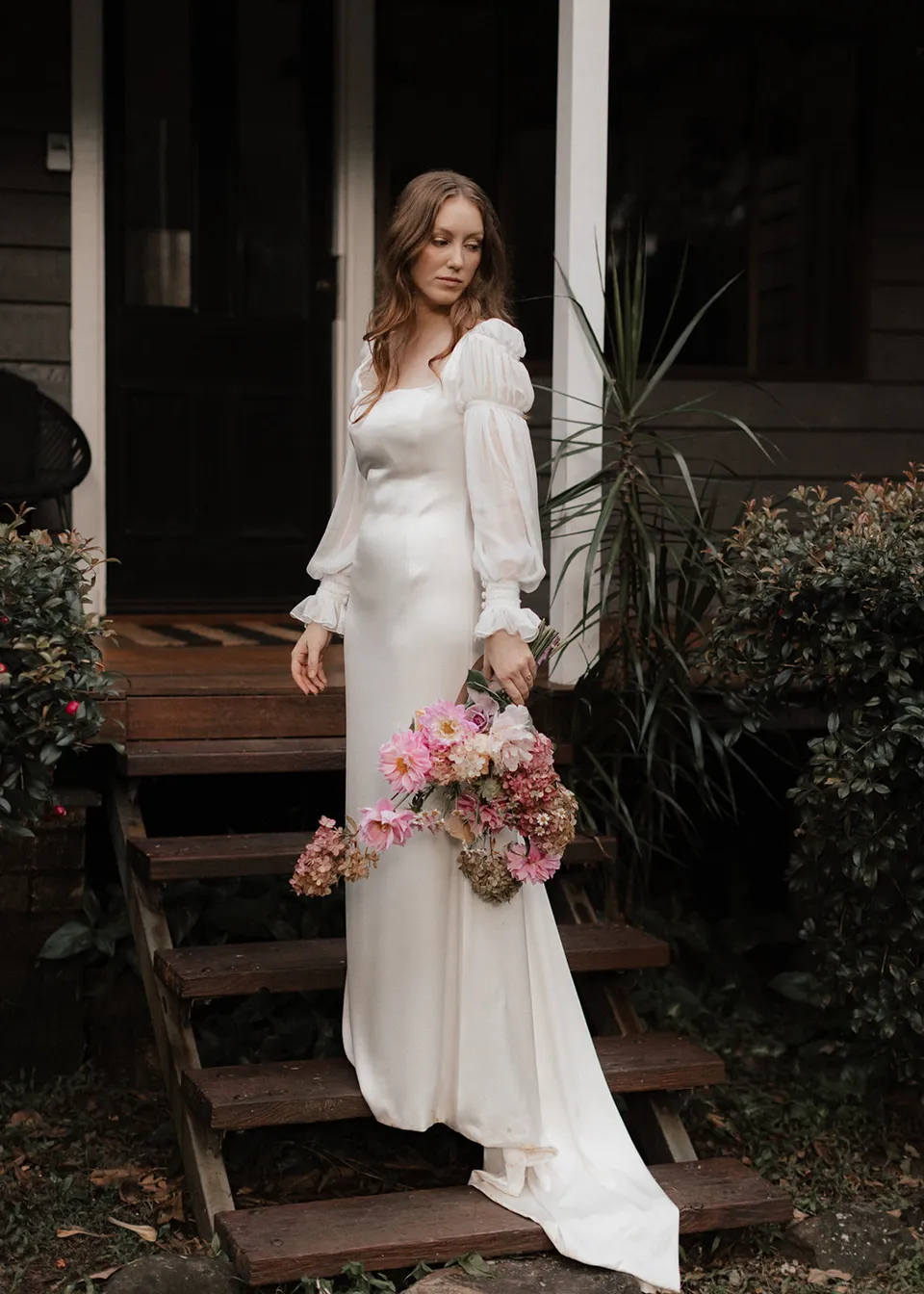 Elyse holding her bouquet outside the weatherboard cottage, with flowers by The Perfect Party Co. At Fig Tree Villa in Ewingsdale, Byron Bay, for an Elopement Collective elopement. Photograph by Bulb Creative.