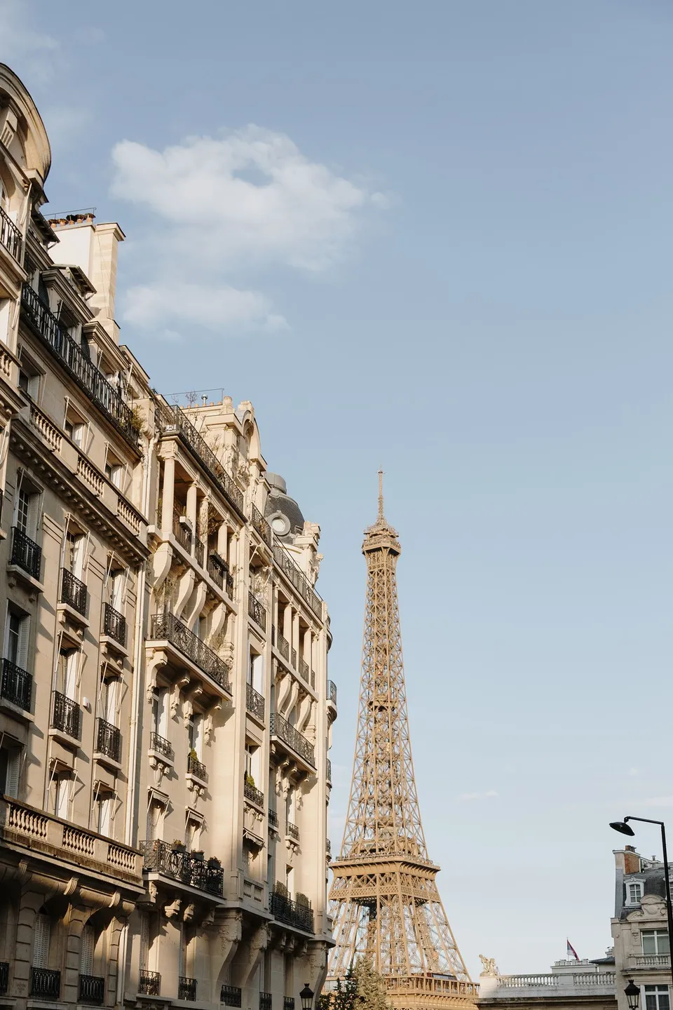 The Eiffel Tower framed between ornate Parisian buildings beneath a blue and cloudy sky, at Avenue de Camoëns in Paris, France, during an Elopement Collective elopement. Photograph by George Bowden.