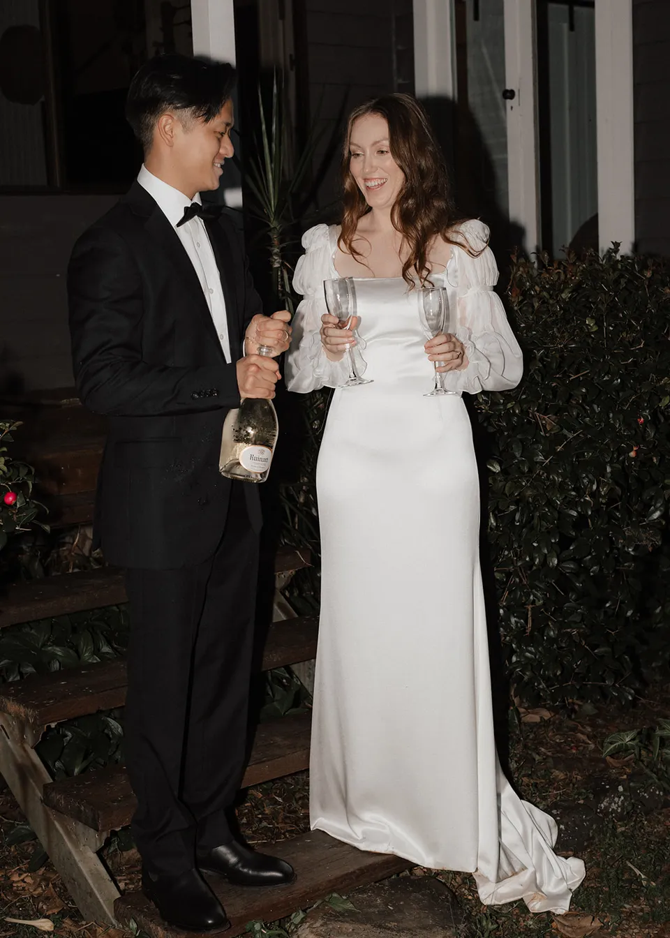 Elyse smiling beside Jonathan as they prepare to toast. At Fig Tree Villa in Ewingsdale, Byron Bay, for an Elopement Collective elopement. Photograph by Bulb Creative.
