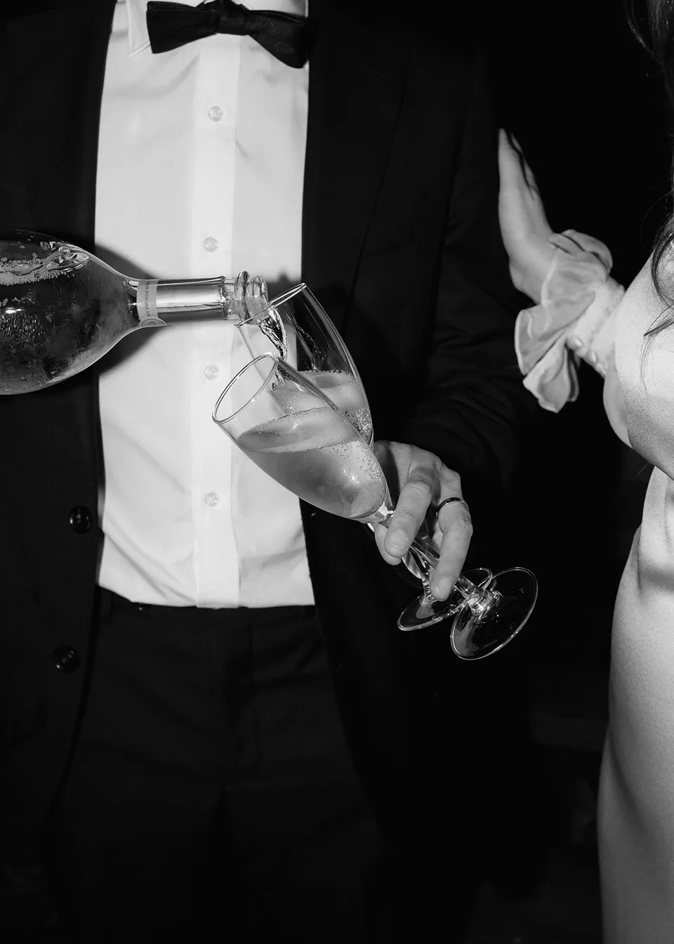 Black-and-white close-up of Jonathan pouring sparkling wine. At Fig Tree Villa in Ewingsdale, Byron Bay, for an Elopement Collective elopement. Photograph by Bulb Creative.