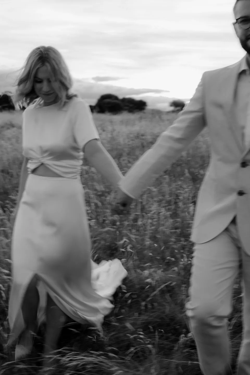 Black and white photograph of Jemmah looking back while holding Jack’s hand, at Thalia Haven on the East Coast of Tasmania, Australia, for an Elopement Collective elopement. Photograph by Joey Willis.