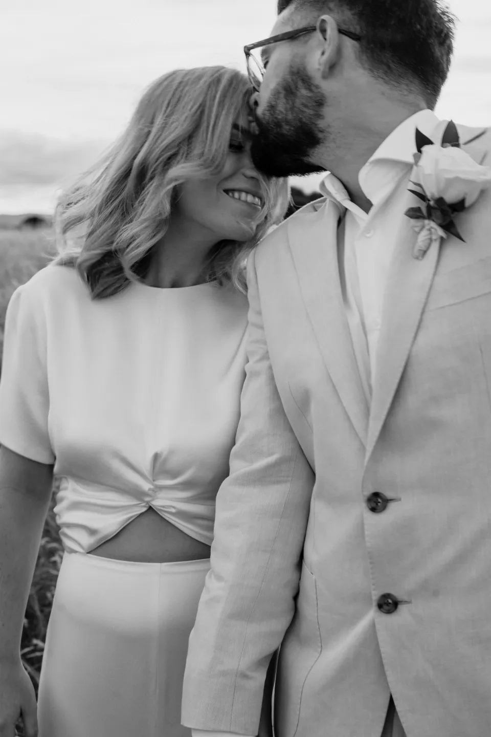 Black and white portrait of Jack kissing Jemmah’s forehead as she laughs, at Thalia Haven on the East Coast of Tasmania, Australia, for an Elopement Collective elopement. Photograph by Joey Willis.