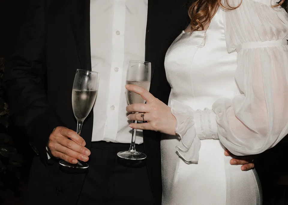Close-up of Elyse and Jonathan's sparkling-wine glasses beside their wedding clothes. At Fig Tree Villa in Ewingsdale, Byron Bay, for an Elopement Collective elopement. Photograph by Bulb Creative.