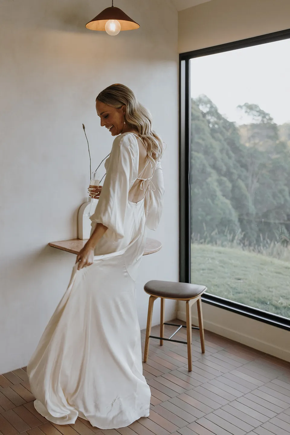 Gabrielle standing beside the cabin’s large window, her ivory dress trailing across the tiled floor at Roundhill Retreat in Obi Obi, Sunshine Coast Hinterland, for their Elopement Collective elopement.
