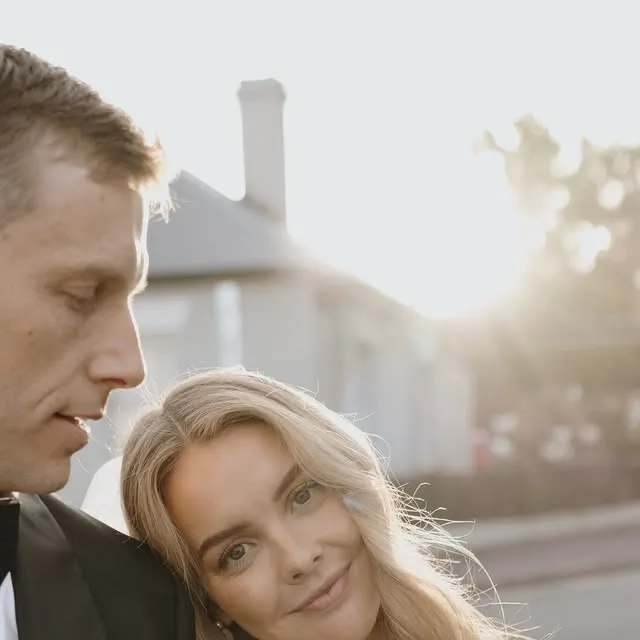 A bride leaning on her partner's arm in warm evening light.