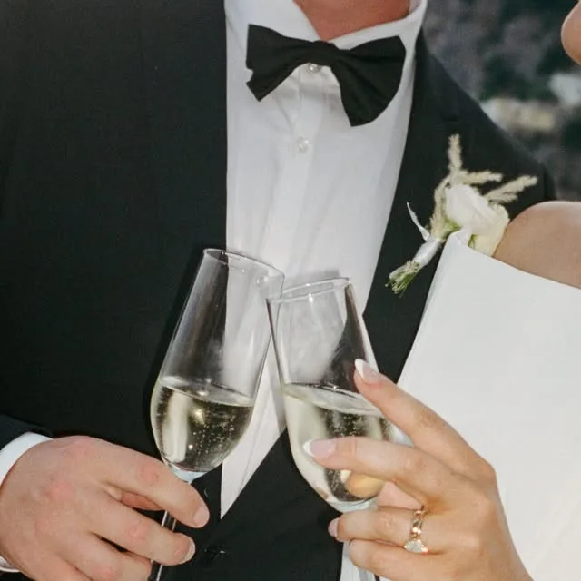 Two people in wedding clothes holding champagne glasses together.