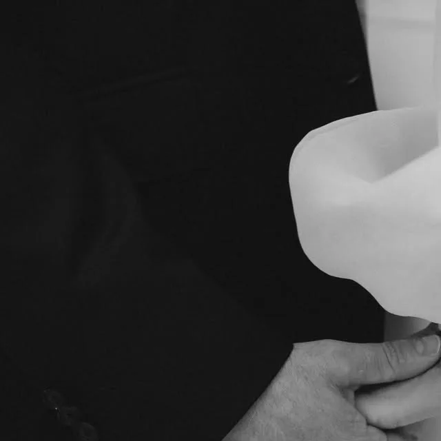 A black-and-white close-up of a hand holding a white wedding dress.