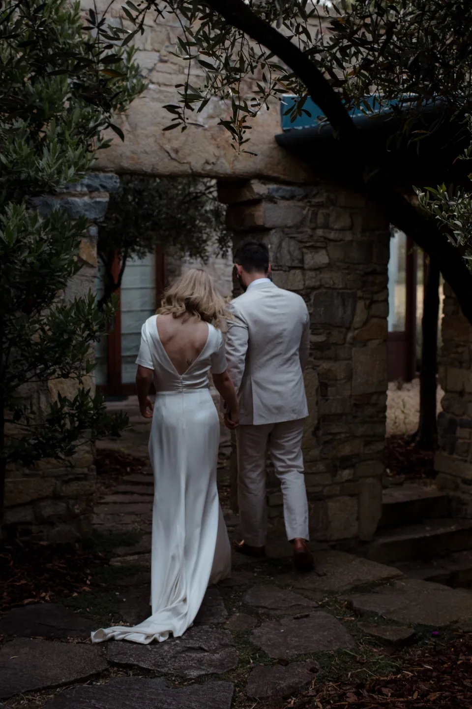 Jemmah and Jack standing close beneath the courtyard trees, at Thalia Haven on the East Coast of Tasmania, Australia, for an Elopement Collective elopement. Photograph by Joey Willis.