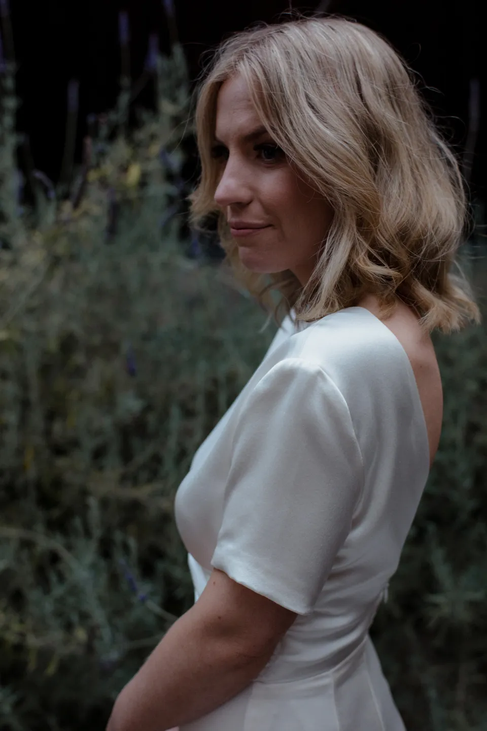 A close portrait of Jemmah looking towards the camera among garden foliage, at Thalia Haven on the East Coast of Tasmania, Australia, for an Elopement Collective elopement. Photograph by Joey Willis.