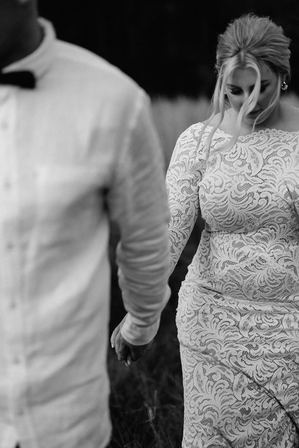 A black and white close-up of Laura looking down as she holds Matt’s hand, showing the intricate lace of her dress, in the Tweed Valley, NSW, for an Elopement Collective elopement. Photo by Bulb Creative.