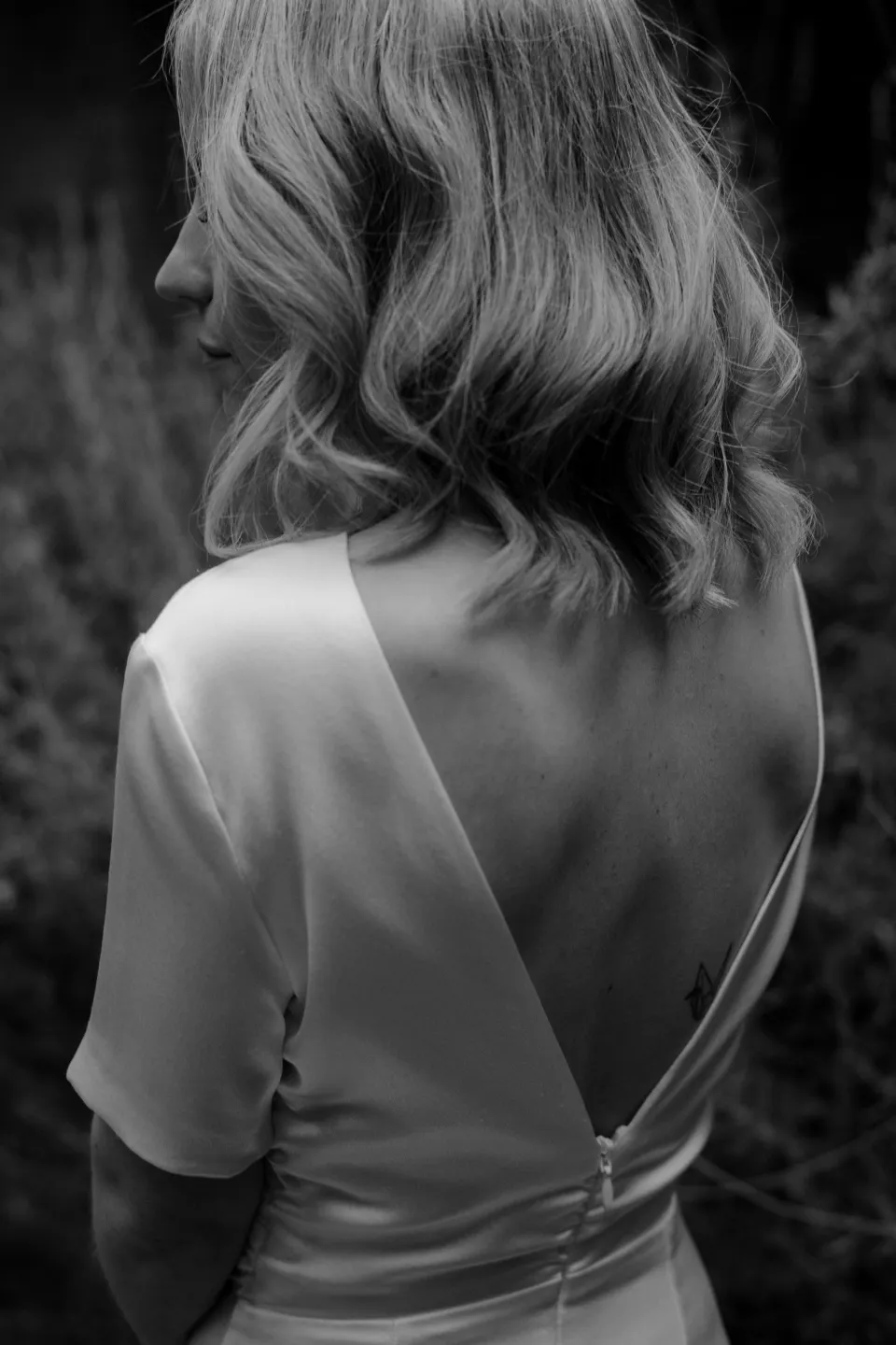 Black and white rear view of Jemmah’s wavy hair and dress neckline, at Thalia Haven on the East Coast of Tasmania, Australia, for an Elopement Collective elopement. Photograph by Joey Willis.