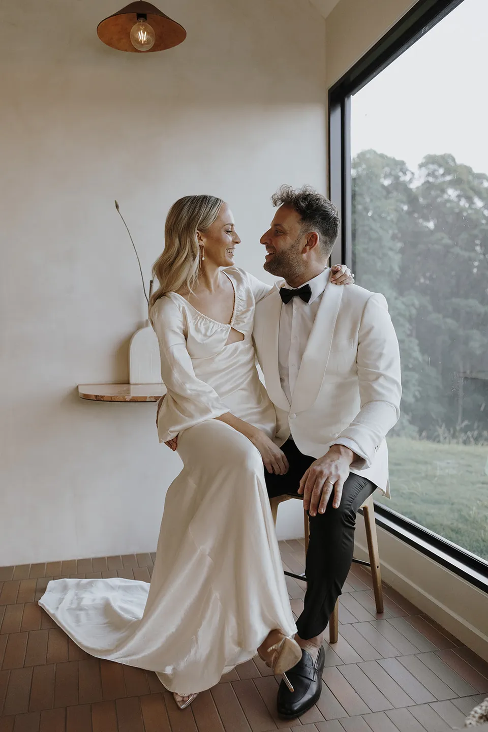 Gabrielle and Greg looking at each other on the window seat beside a broad view of the hinterland at Roundhill Retreat in Obi Obi, Sunshine Coast Hinterland, for their Elopement Collective elopement.