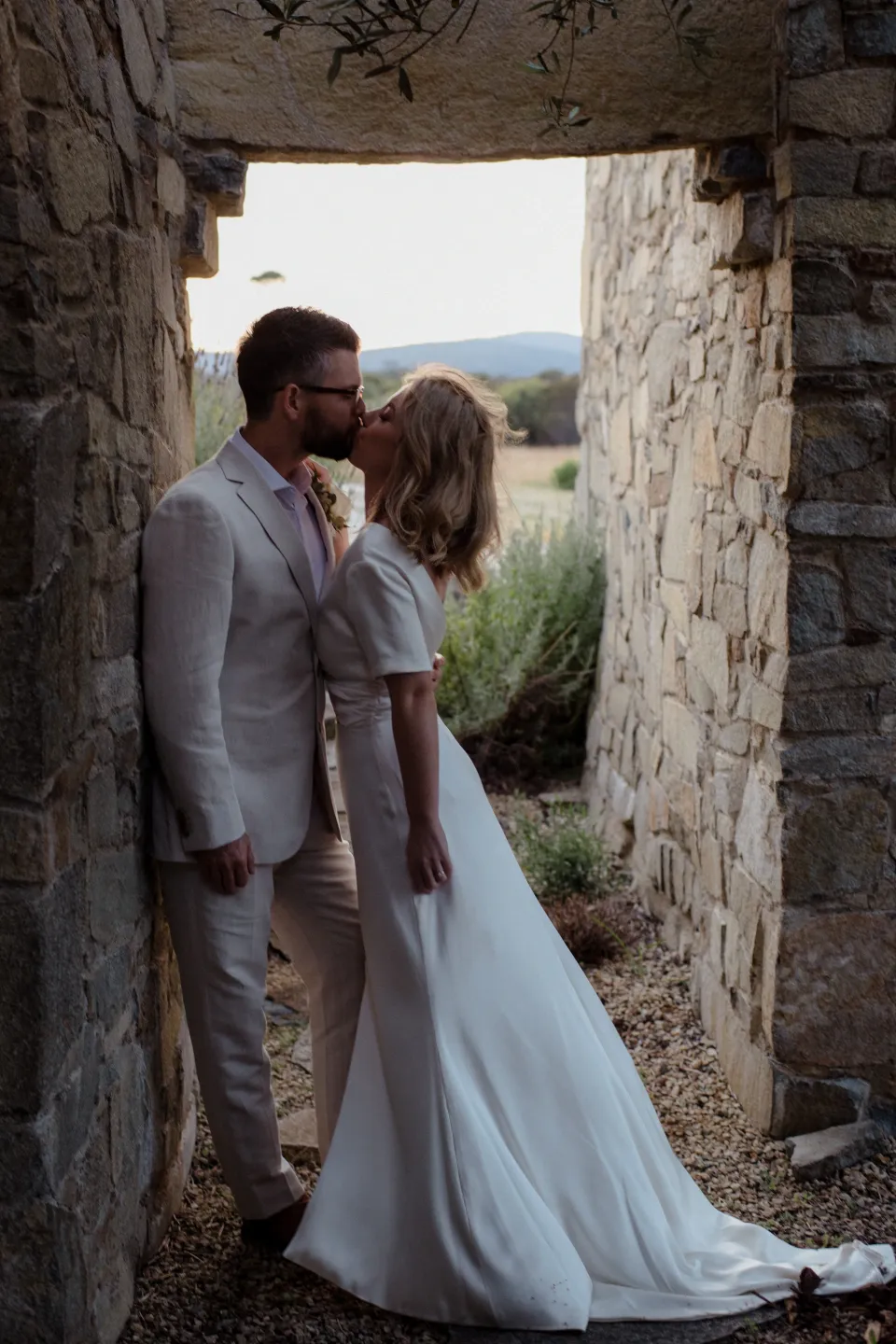 Jemmah and Jack framed by a narrow stone doorway, at Thalia Haven on the East Coast of Tasmania, Australia, for an Elopement Collective elopement. Photograph by Joey Willis.
