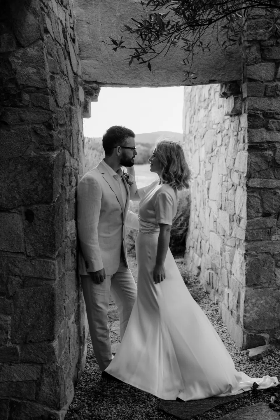 Black and white photograph of the couple standing together in the stone doorway, at Thalia Haven on the East Coast of Tasmania, Australia, for an Elopement Collective elopement. Photograph by Joey Willis.