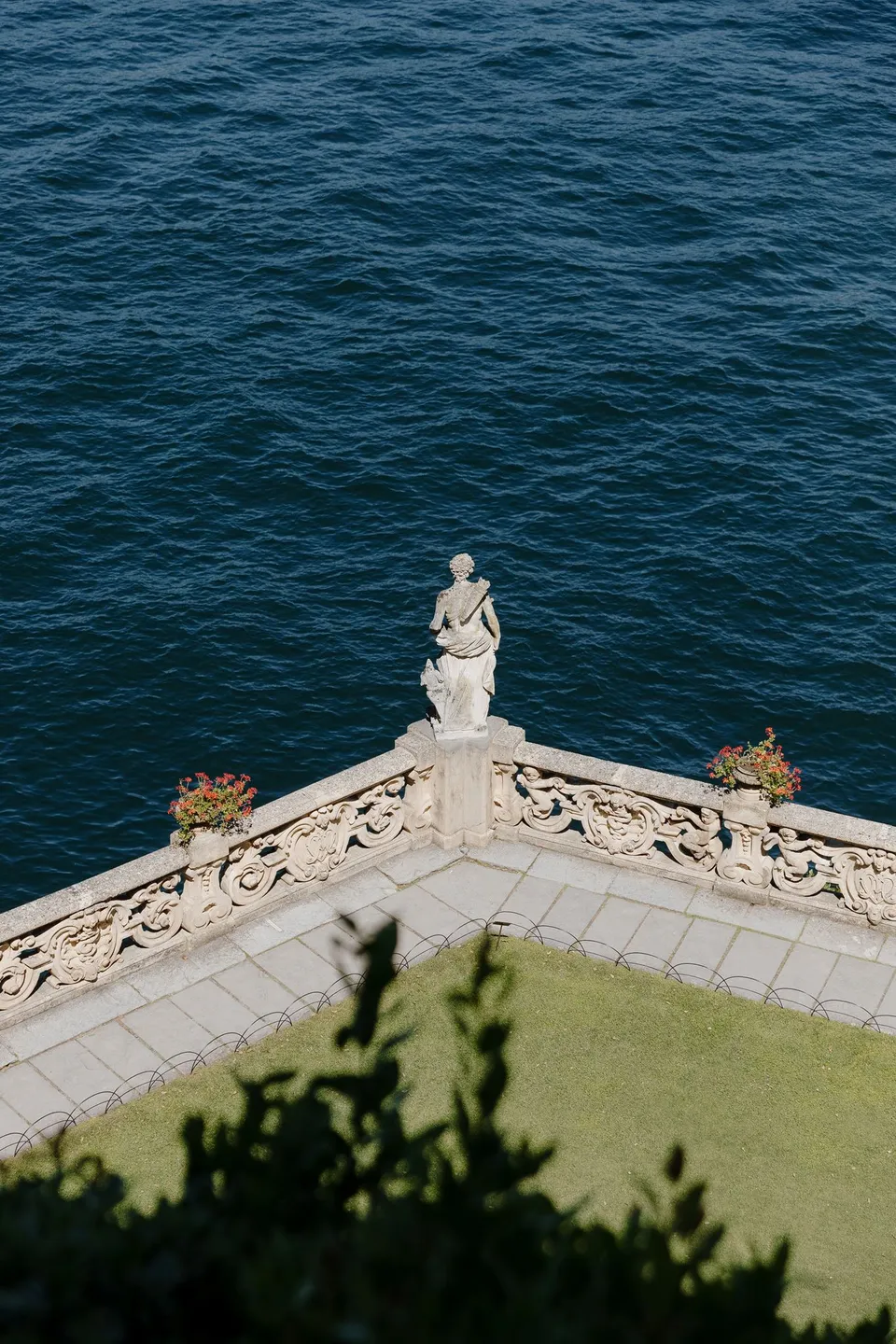 A classical statue and stone balustrade on a terrace at Villa del Balbianello above deep blue lake water, at Lake Como in Lombardy, Italy, for an Elopement Collective elopement. Photograph by George Bowden.