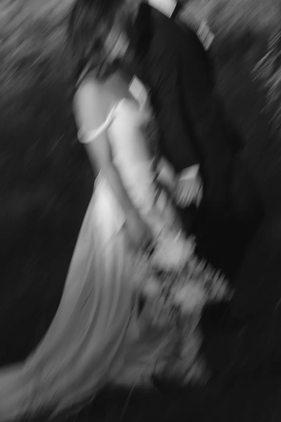 A black and white portrait with intentional motion blur of Clara and Harry embracing, with her bouquet by The Romantics, at Thalia Haven on the East Coast of Tasmania, for an Elopement Collective elopement. Photograph by Bulb Creative.