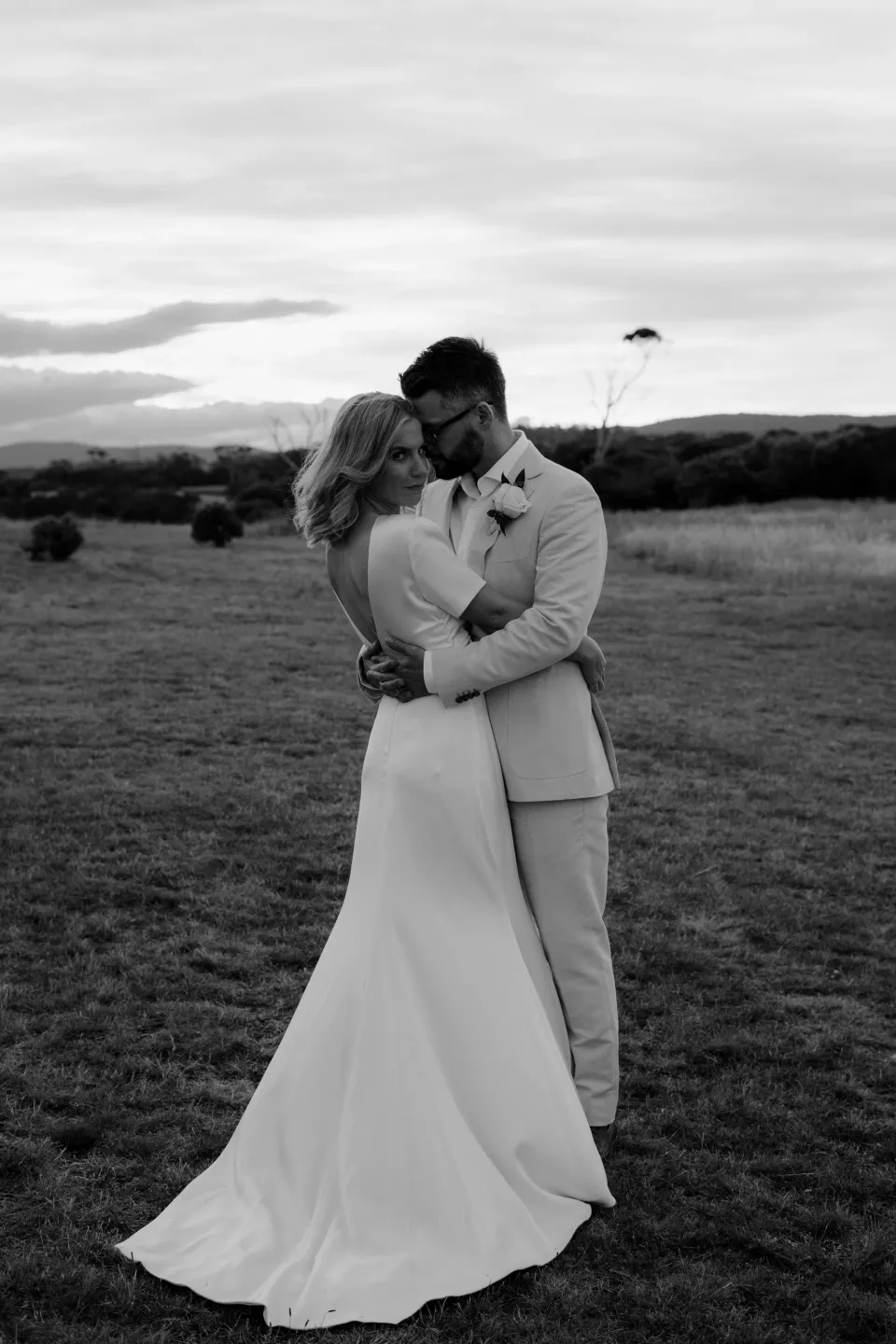 Black and white portrait of the couple kissing beneath the evening sky, at Thalia Haven on the East Coast of Tasmania, Australia, for an Elopement Collective elopement. Photograph by Joey Willis.