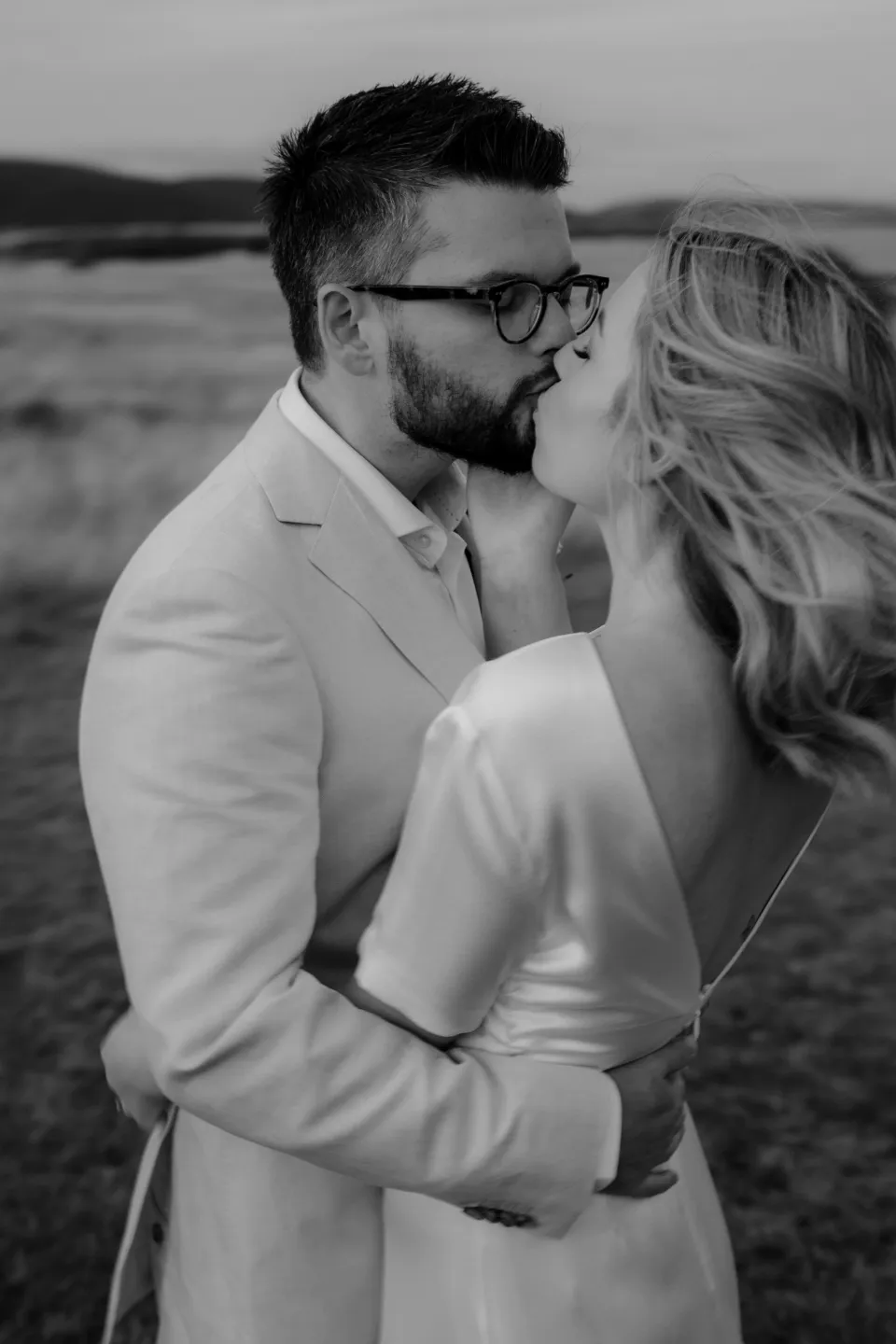 Black and white portrait of the couple kissing in the meadow, at Thalia Haven on the East Coast of Tasmania, Australia, for an Elopement Collective elopement. Photograph by Joey Willis.