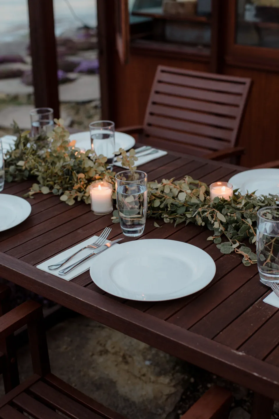 Candles, plates and greenery arranged on the outdoor dining table, at Thalia Haven on the East Coast of Tasmania, Australia, for an Elopement Collective elopement. Photograph by Joey Willis.