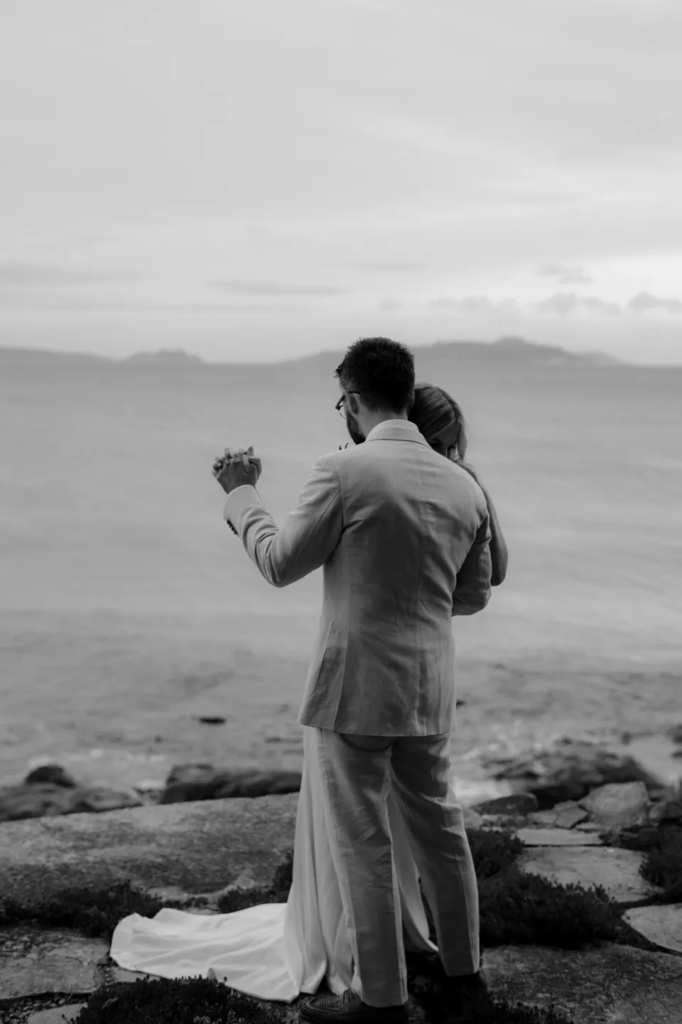Black and white photograph of Jack holding Jemmah on the stone terrace, at Thalia Haven on the East Coast of Tasmania, Australia, for an Elopement Collective elopement. Photograph by Joey Willis.