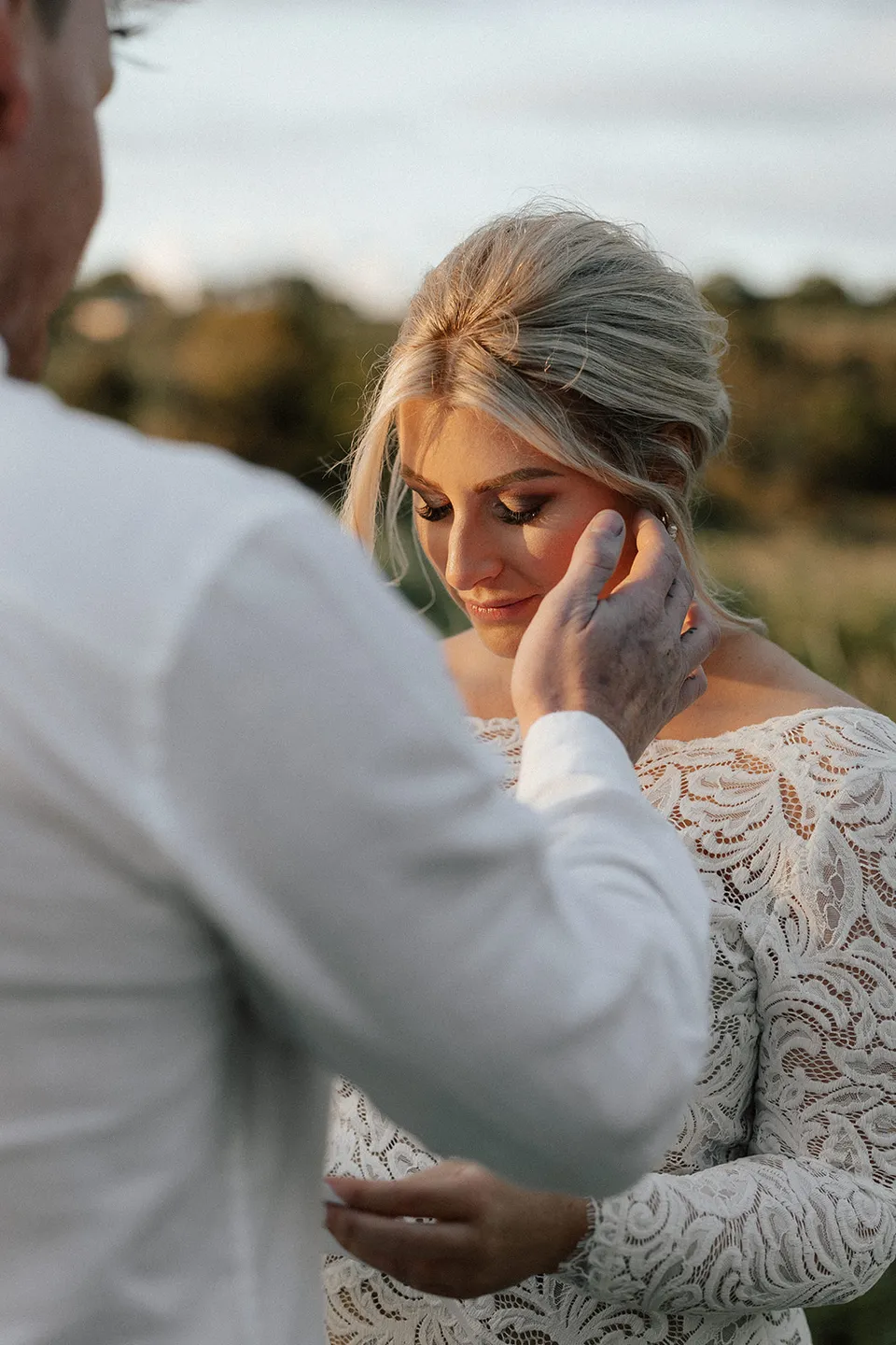 Matt gently touching Laura’s cheek as she looks down during their ceremony in the evening light, in the Tweed Valley, NSW, for an Elopement Collective elopement. Photo by Bulb Creative.